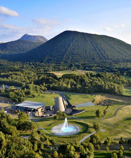 Vue aérienne de Vulcania, le parc de découverte des volcans, entouré de paysages verdoyants et de volcans, avec une fontaine au premier plan