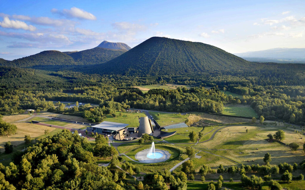 Vue aérienne de Vulcania, le parc de découverte des volcans, entouré de paysages verdoyants et de volcans, avec une fontaine au premier plan